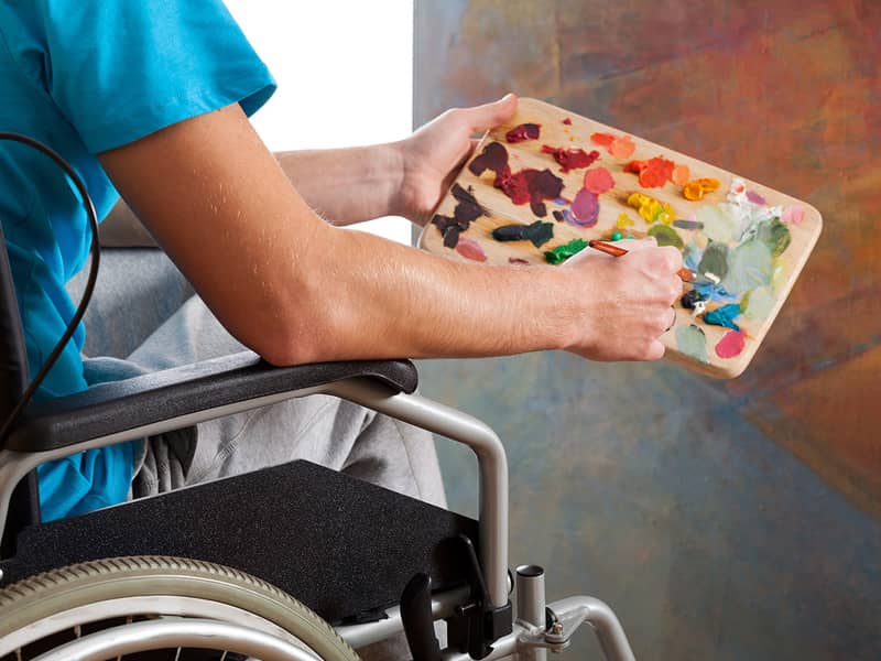 Ein Rollstuhlfahrer nutzt Pinsel und Farbpalette